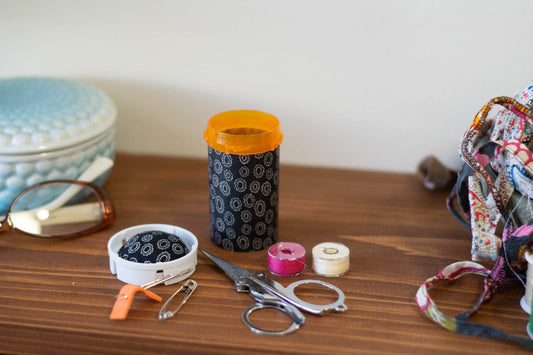 upcycled prescription bottle sewing kit — small white rings on black, 3" high, open with contents